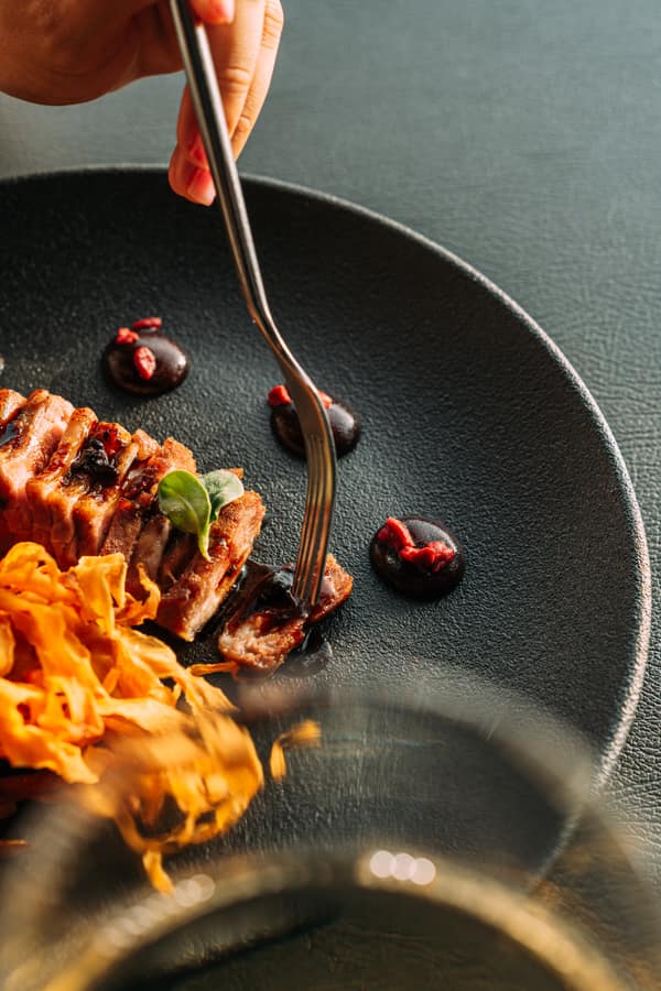 Meat with reduction and red fruits on black ceramic