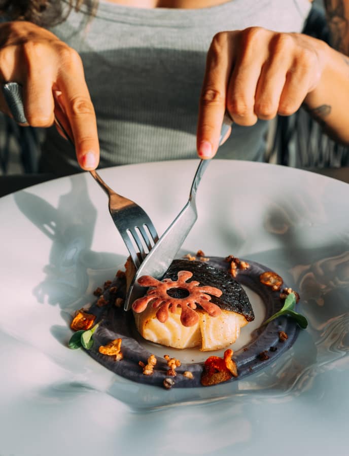 Fish with squid-ink garnish on a white plate
