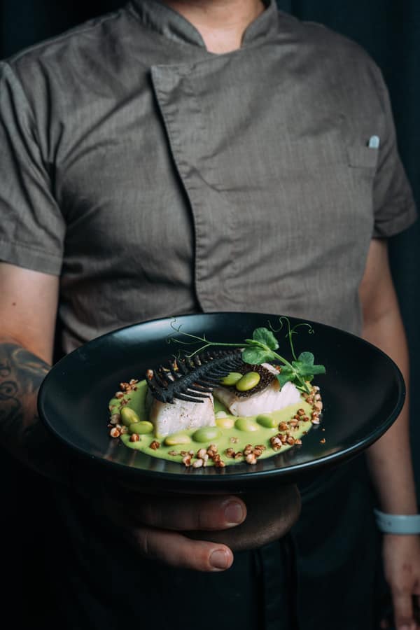 Chef presenting a fish dish with peas